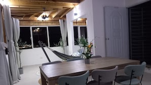 Een eethoek met een houten tafel en vier stoelen, een hangmat en een bloeiende plant in een pot.