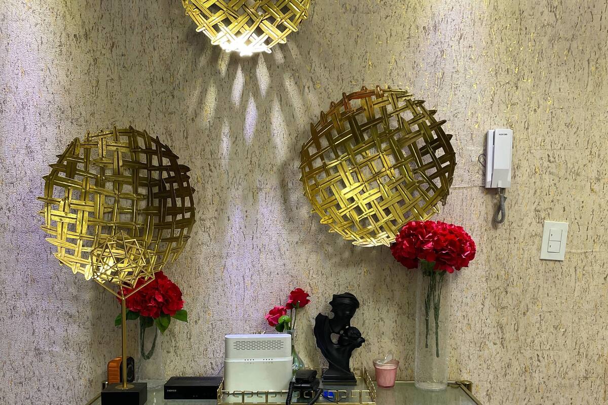 Une table avec un plateau en verre et des pieds dorés, un téléphone, un vase avec des fleurs rouges et deux sphères décoratives dorées sur un mur texturé.