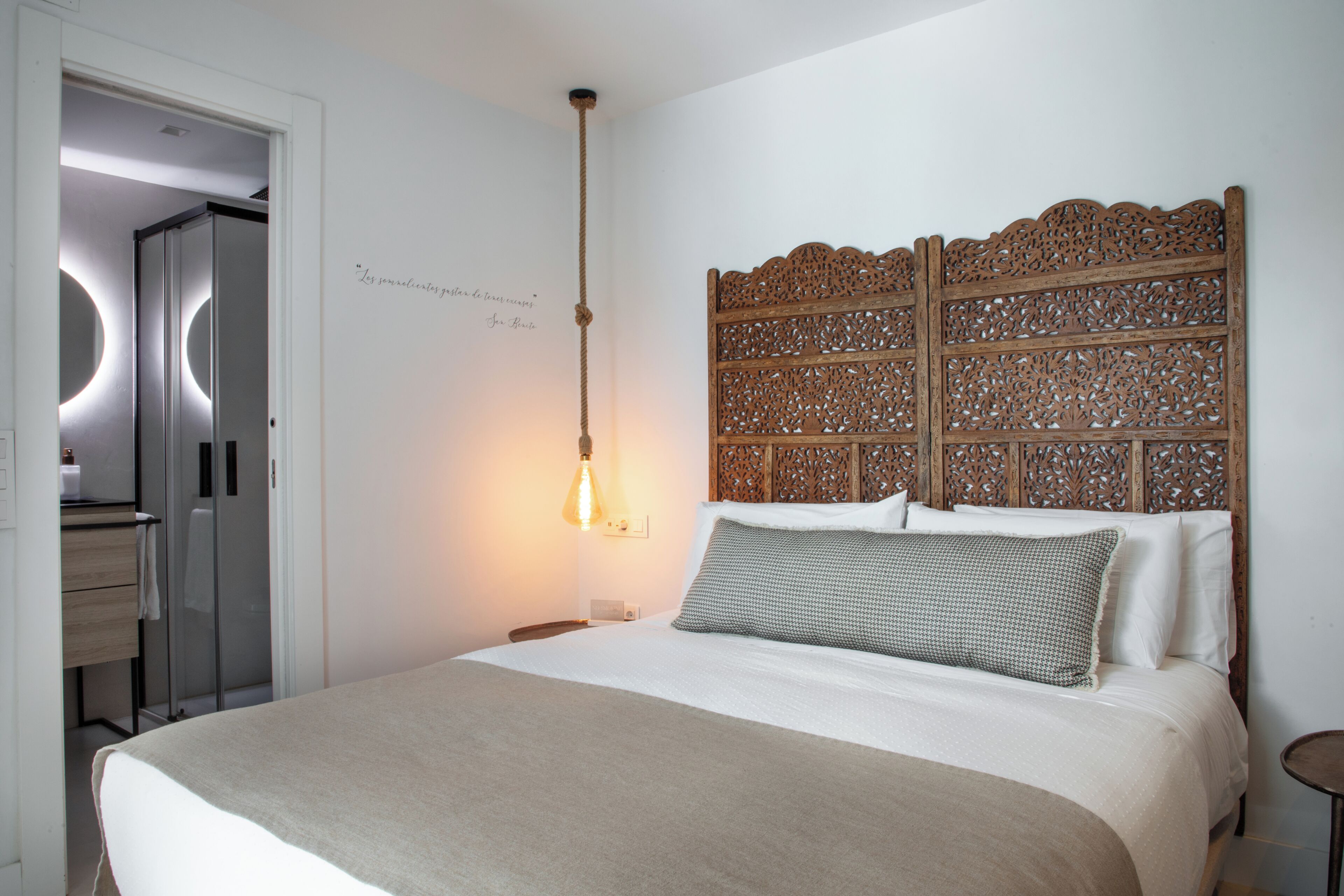 Un dormitorio con cama, cabecera de madera, lámpara de noche y puerta que da al baño.