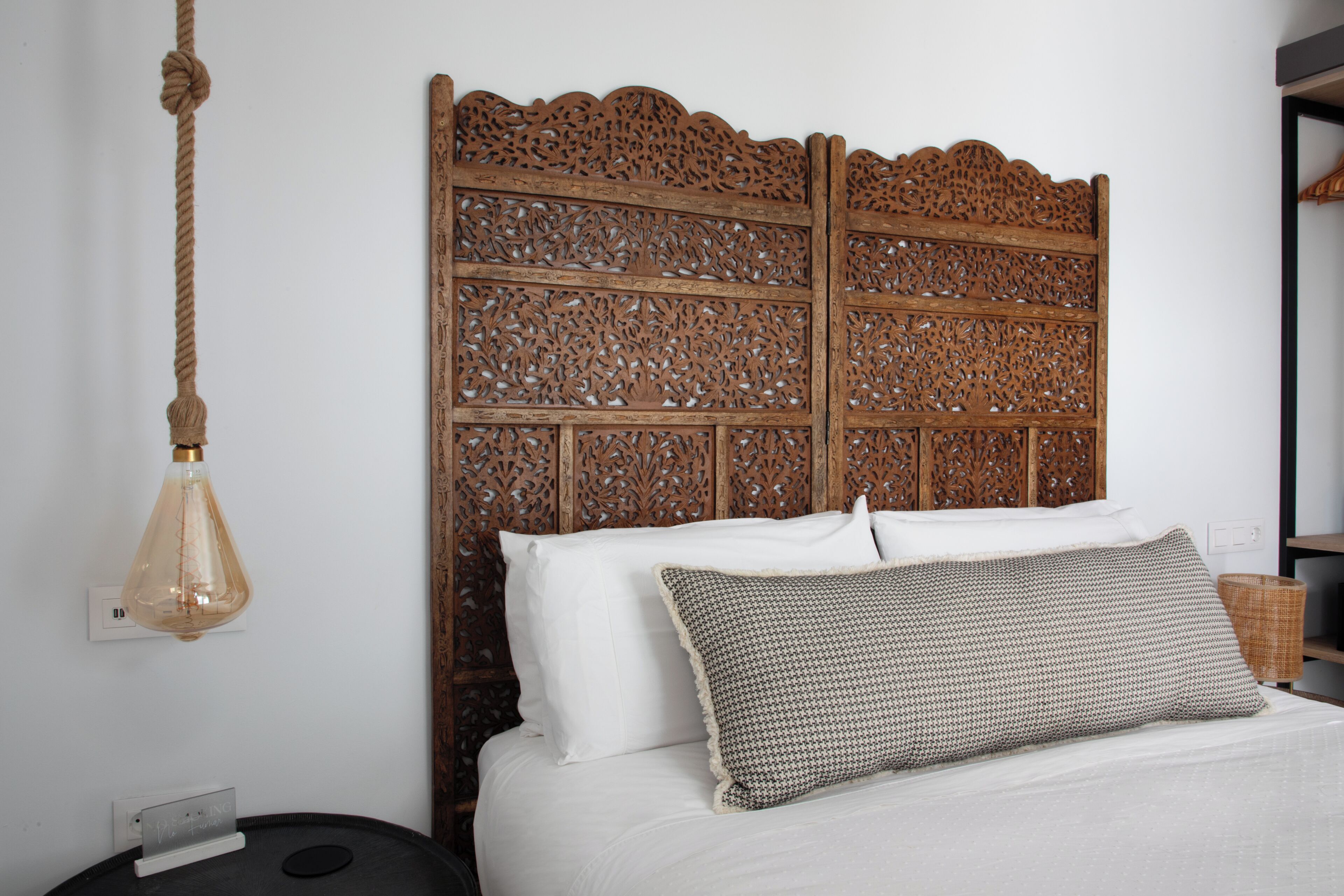 Un lit avec une literie blanche, un oreiller à motifs et une tête de lit en bois ornée de sculptures complexes.
