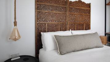 Un lit avec une literie blanche, un oreiller à motifs et une tête de lit en bois ornée de sculptures complexes.
