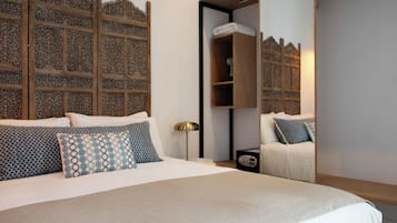 Un dormitorio ordenado con una cama grande, una mesita de noche con lámpara y un armario de madera con panel decorativo.