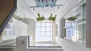 Un interno moderno con una finestra centrale, ringhiere in vetro e un soffitto decorato con piante pensili.