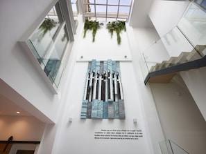 A modern interior with a high ceiling, glass railings, and a large abstract art piece on the wall.