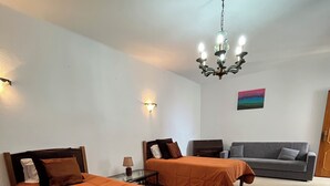 Een hotelkamer met twee bedden, een grijze bank, een kroonluchter en een schilderij aan de muur.