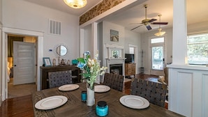 A dining room with a wooden table set for six, a vase with flowers, and a fireplace in the background. - Magnolia Beach House l Brand NEW AC UNIT (Gulfport)