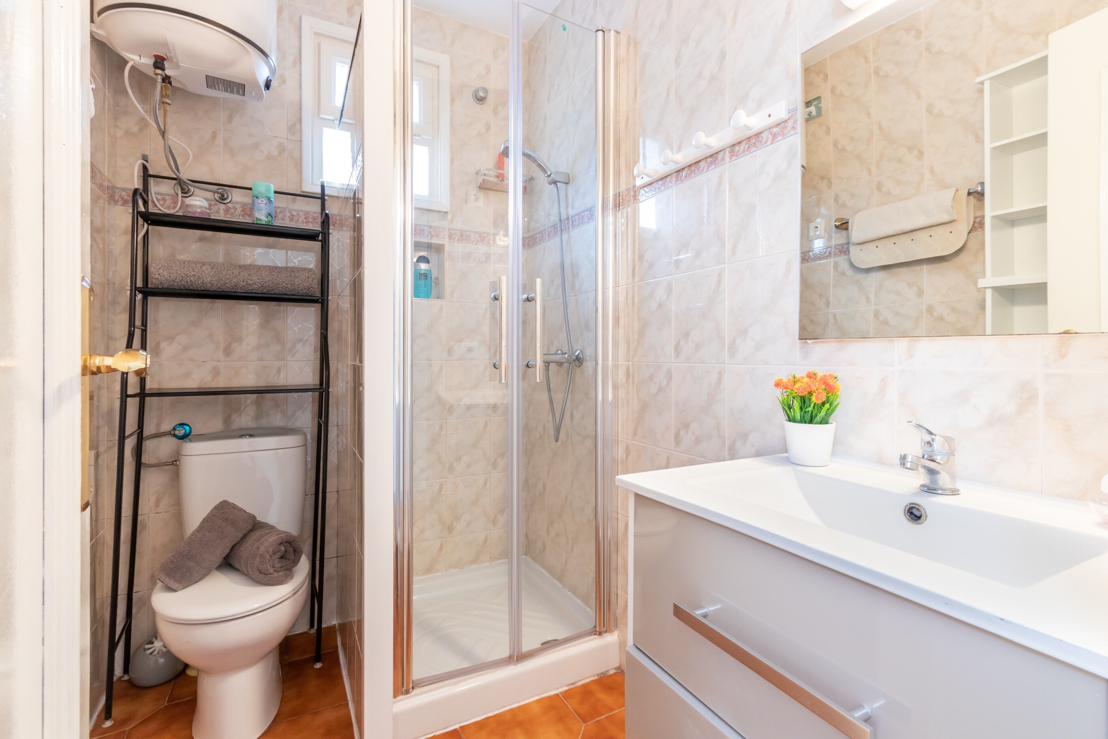 Un baño con ducha de vidrio, inodoro, lavamanos con espejo y repisa con artículos de aseo.