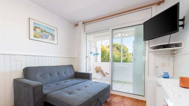 Un soggiorno moderno con un divano grigio, una TV a schermo piatto e una porta vetrata scorrevole che dà su un balcone.