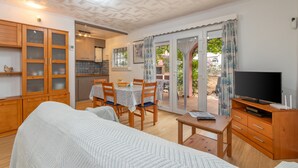 A room with a bed, a television, a dining table with chairs, a kitchen area, and a sliding glass door leading to an outdoor patio. - Holiday Home 'Giovanni' with Shared Terrace and Wi-Fi (L'Escala)