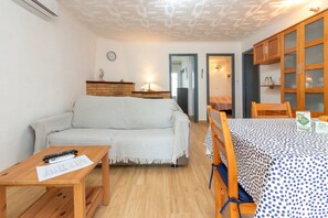 A cozy living room with a sofa, a wooden table with papers, a dining table with a polka dot tablecloth, and a brick fireplace. - Holiday Home 'Giovanni' with Shared Terrace and Wi-Fi (L'Escala)