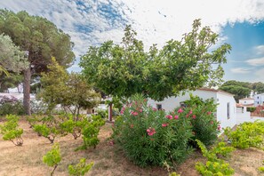 A white building with a red roof, surrounded by a garden with various plants and trees. - Holiday Home 'Giovanni' with Shared Terrace and Wi-Fi (L'Escala)