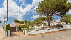 A residential area with a large tree, a white wall with a decorative fence, and a clear sky. - Holiday Home 'Giovanni' with Shared Terrace and Wi-Fi (L'Escala)