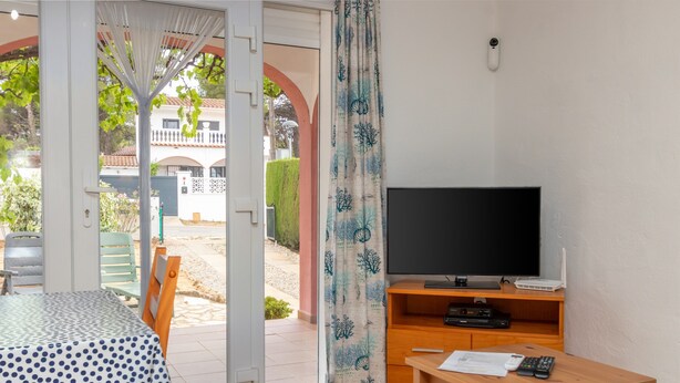A room with a TV, wooden furniture, a table with papers, and a view through an open door. - Holiday Home 'Giovanni' with Shared Terrace and Wi-Fi (L'Escala)