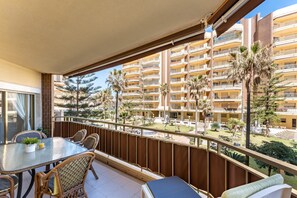 A balcony with a table and chairs, overlooking a building with multiple balconies and palm trees. - Holiday Apartment "Doña Sofía" with Sea View, Private Terraces & Wi-Fi (Fuengirola)