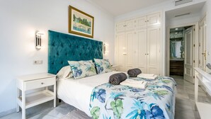 A bedroom with a bed, nightstand, wardrobe, and a painting on the wall.