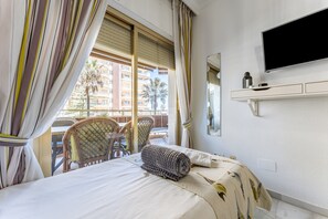 A hotel room with a bed, a television, a window with curtains, a chair, and a balcony view. - Holiday Apartment "Doña Sofía" with Sea View, Private Terraces & Wi-Fi (Fuengirola)