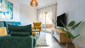 A modern living room with a sofa, armchair, TV, and a large plant.