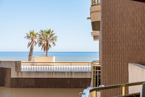 Een balkon met uitzicht op zee, palmbomen en een bakstenen gebouw.