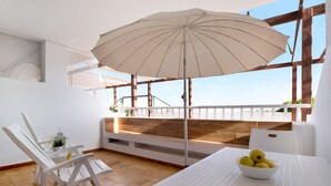 Una habitación con una mesa blanca, una silla blanca, un banco blanco, un paraguas blanco y un cuenco de fruta.