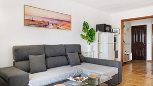 Una sala de estar con un sofá, una mesa de centro de vidrio, una planta y un cuadro en la pared.