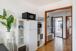 A compact kitchen with a microwave, a refrigerator, and a potted plant.