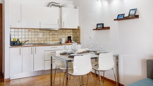 Una cocina moderna con armarios blancos, un salpicadero de azulejos y un comedor con mesa de vidrio y sillas blancas.