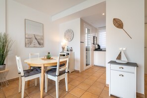 Un coin repas comprenant une table ronde, deux chaises, une plante en pot, une horloge murale et un meuble avec des tiroirs.