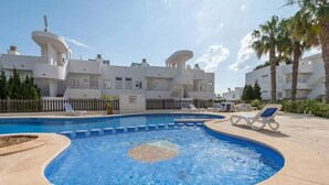 A swimming pool with lounge chairs, a white building with unique architecture, and a clear sky. - Apartment 'El Puerto I 1-3' with Shared Pool, Wi-Fi and Air Conditioning (Cala D'or)