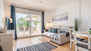 A modern living room with a sofa, a dining table, and a large sliding glass door leading to an outdoor patio. - Apartment 'El Puerto I 1-3' with Shared Pool, Wi-Fi and Air Conditioning (Cala D'or)