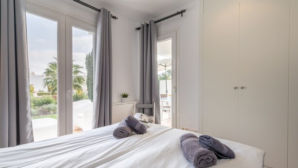 A hotel room with a bed, two rolled towels, a desk, and a view of the outdoors. - Apartment 'El Puerto I 1-3' with Shared Pool, Wi-Fi and Air Conditioning (Cala D'or)