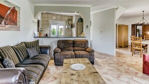 A living room with a sofa, a chair, a coffee table, and a dining area with chairs and a table. - Villa 'Casa Flores' with Mountain Views, Shared Pool, and Wi-Fi (Vilacolum)