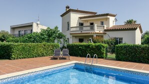 A swimming pool with lounge chairs, a two-story building with a balcony, and a clear sky. - Villa 'Casa Flores' with Mountain Views, Shared Pool, and Wi-Fi (Vilacolum)