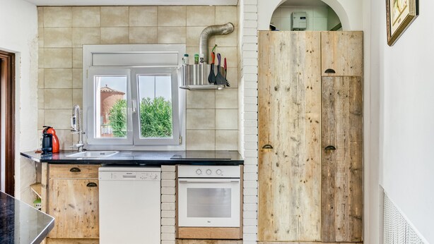 A kitchen with a window, a dishwasher, an oven, and a wooden door. - Villa 'Casa Flores' with Mountain Views, Shared Pool, and Wi-Fi (Vilacolum)