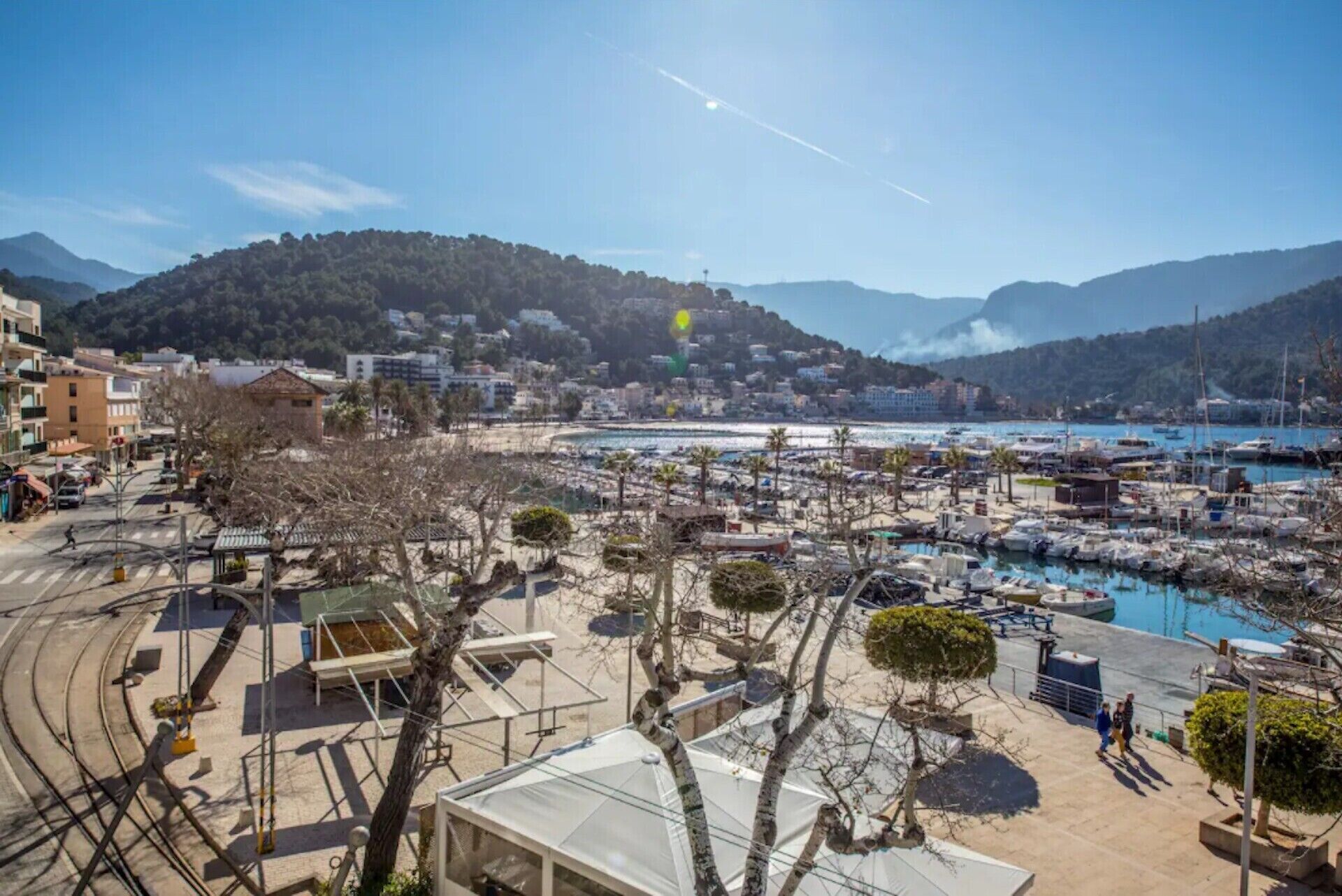 A marina with boats, a clear sky, and a hilly landscape in the background.