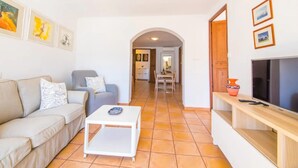 A living room with a sofa, a coffee table, a TV, and a dining area with chairs and a table. - Holiday Apartment Ca Na Magda with Sea View, Wi-Fi, A/C & Balcony (Port de Sóller)