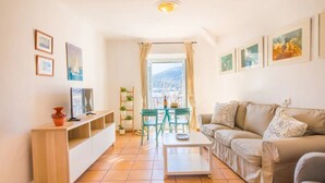 A living room with a sofa, a coffee table, a TV, a small table with chairs, and a view of the outdoors. - Holiday Apartment Ca Na Magda with Sea View, Wi-Fi, A/C & Balcony (Port de Sóller)