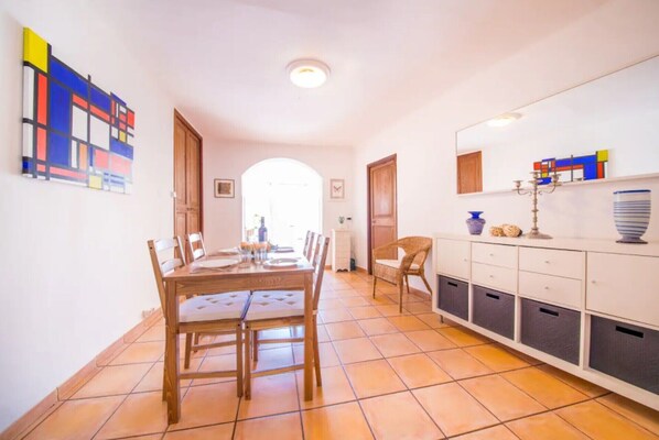 A dining area with a wooden table and chairs, a white cabinet with drawers, and a colorful abstract painting on the wall.