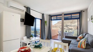 A modern living room with a sofa, dining table set, and a TV. - Vacation Apartment 'Paraíso Taurito' with Sea View, Terrace, Shared Pool & Wi-Fi (Taurito)