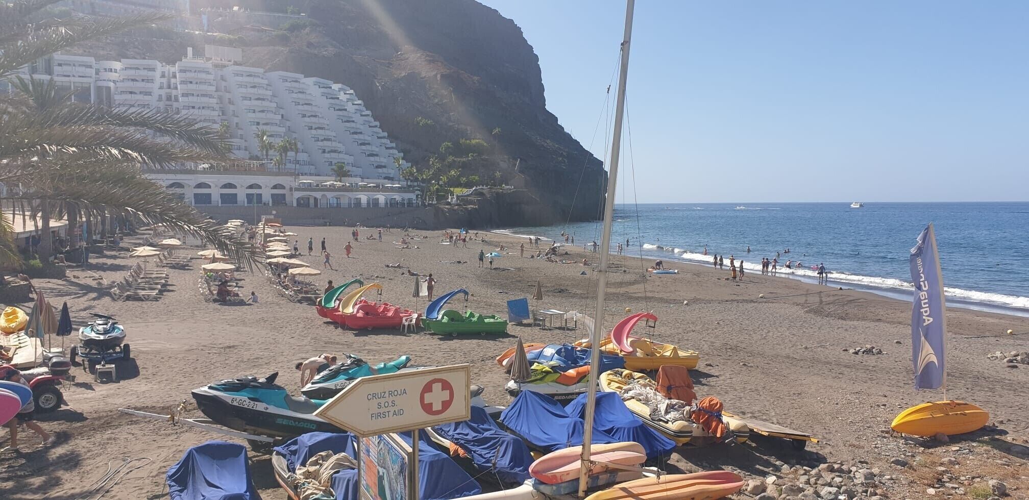 A beach with boats, a lifeguard sign, and a building in the background.