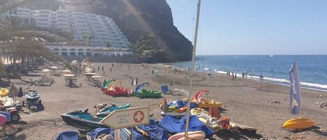 A beach with boats, a lifeguard sign, and a building in the background.