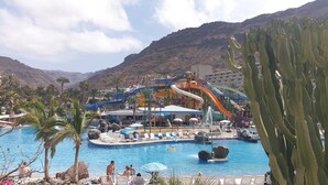 A resort with a pool, water slides, palm trees, and a mountain backdrop. - Vacation Apartment 'Paraíso Taurito' with Sea View, Terrace, Shared Pool & Wi-Fi (Taurito)