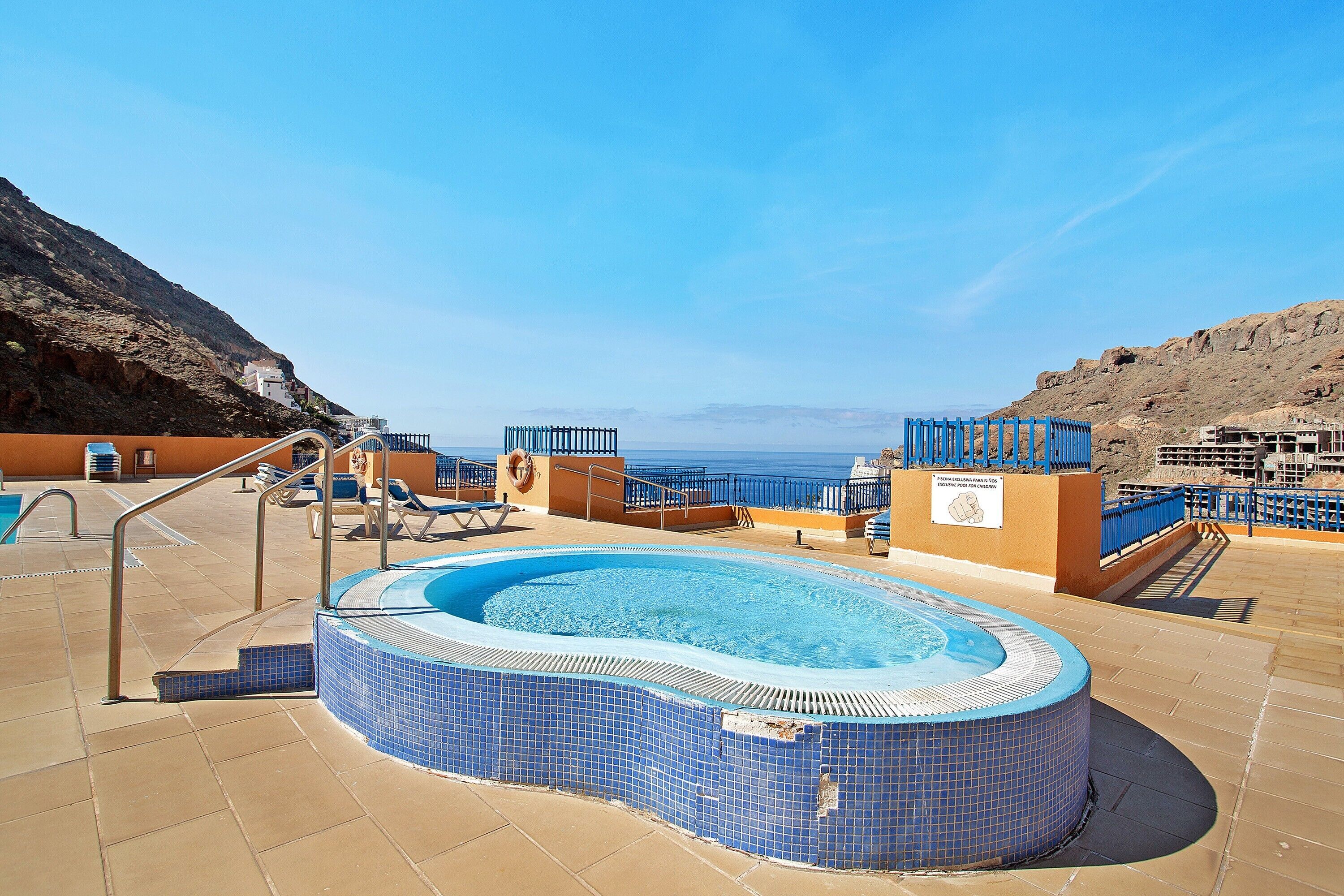 A pool area with a hot tub, lounge chairs, and a view of the sea.