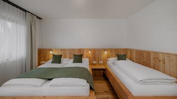 Une chambre avec deux lits, des têtes de lit en bois, du linge de lit blanc et une fenêtre ornée de rideaux légers.