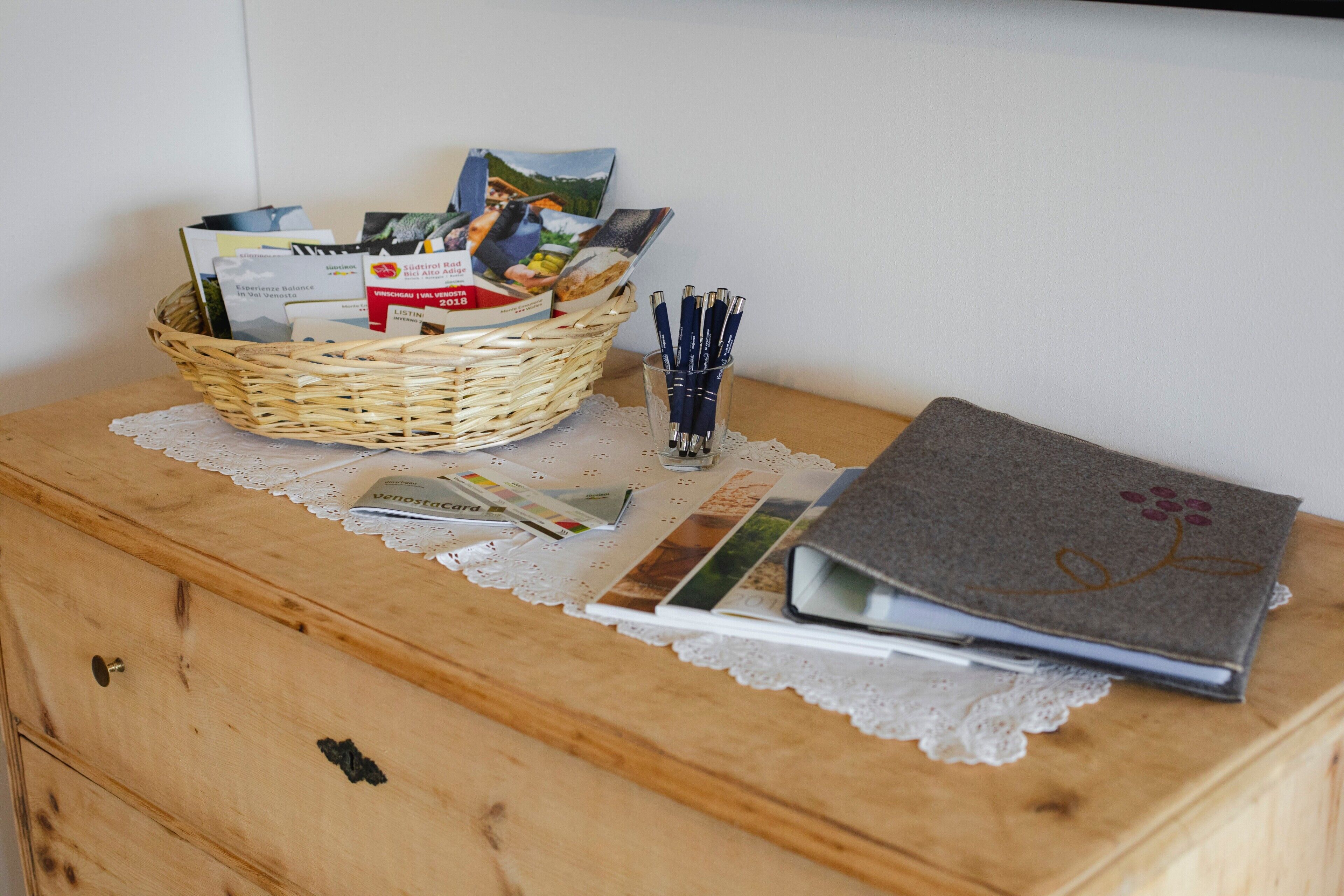 Un comò in legno con un cesto di vimini che contiene brochure e un portapenne.