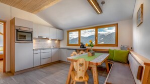 A modern kitchen with wooden cabinets, a built-in oven, and a dining area with a bench and table. - Apartment 'Vernalhof Apt Panorama' with Mountain View, Shared Terrace and Wi-Fi (Sluderno)