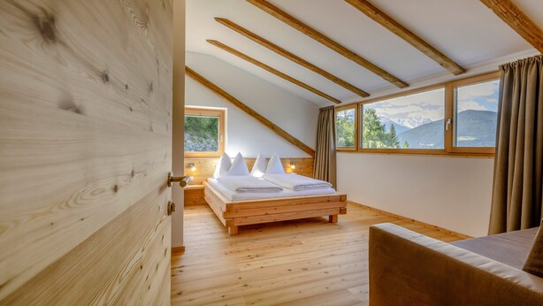A bedroom with a wooden floor, a bed with white linens, a wooden ceiling, and a window with a mountain view. - Apartment 'Vernalhof Apt Panorama Large' with Mountain View, Shared Terrace and Wi-Fi (Sluderno)