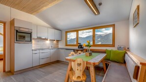 A modern kitchen with wooden cabinets, a built-in oven, and a dining area with a wooden table and bench. - Apartment 'Vernalhof Apt Panorama Large' with Mountain View, Shared Terrace and Wi-Fi (Sluderno)