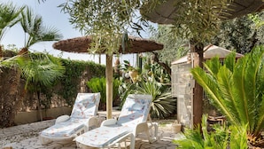 A patio with lounge chairs, a thatched umbrella, and a variety of plants. - Studio 'Alojamiento Ruizo' with Mountain Views, Shared Pool and Wi-Fi (Lorca)