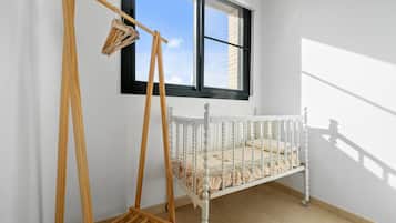 Een wit kinderbed met een gevlinderd matras, een houten schommel en een raam met zwarte kozijnen.