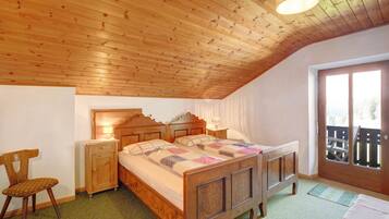 A bedroom with a wooden ceiling, a bed with a quilt, a nightstand, a chair, and a window with a view.
